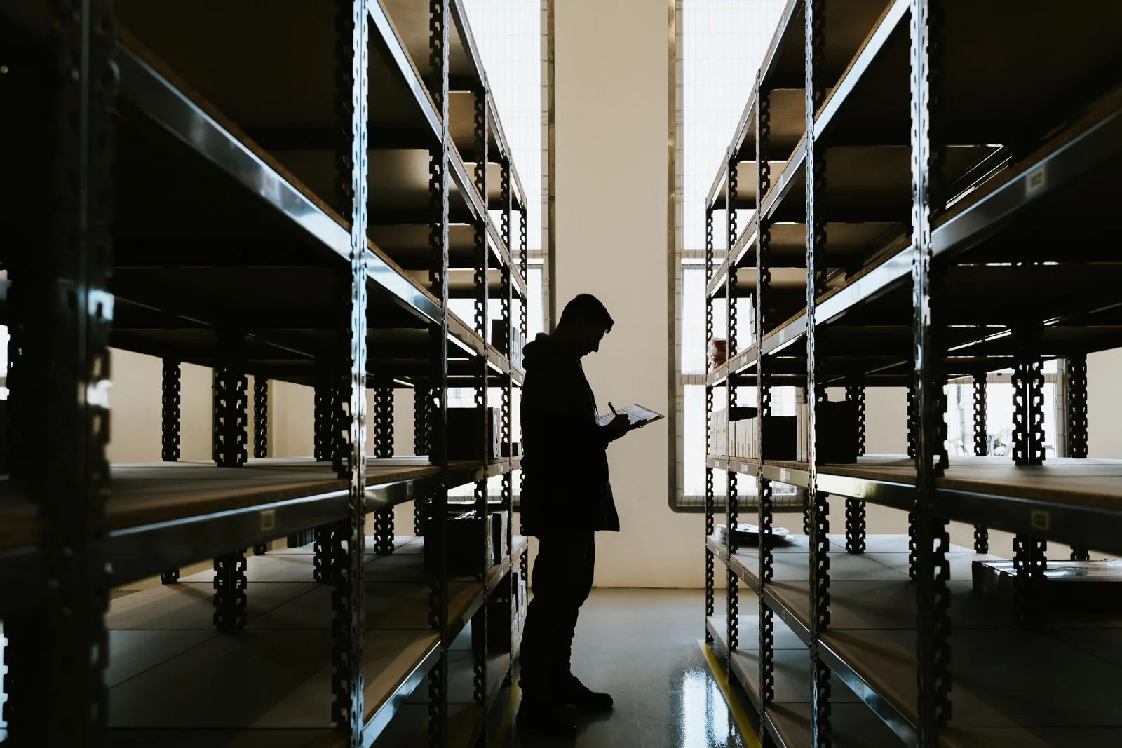 Procurement coordinator checking supplier and inventory records in a warehouse.